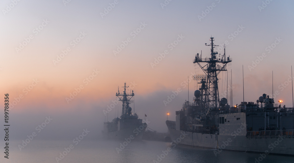 A background of a war ship in the naval base during sunset. Some navy ships in the sea with a marvelous orange light in the sky. 