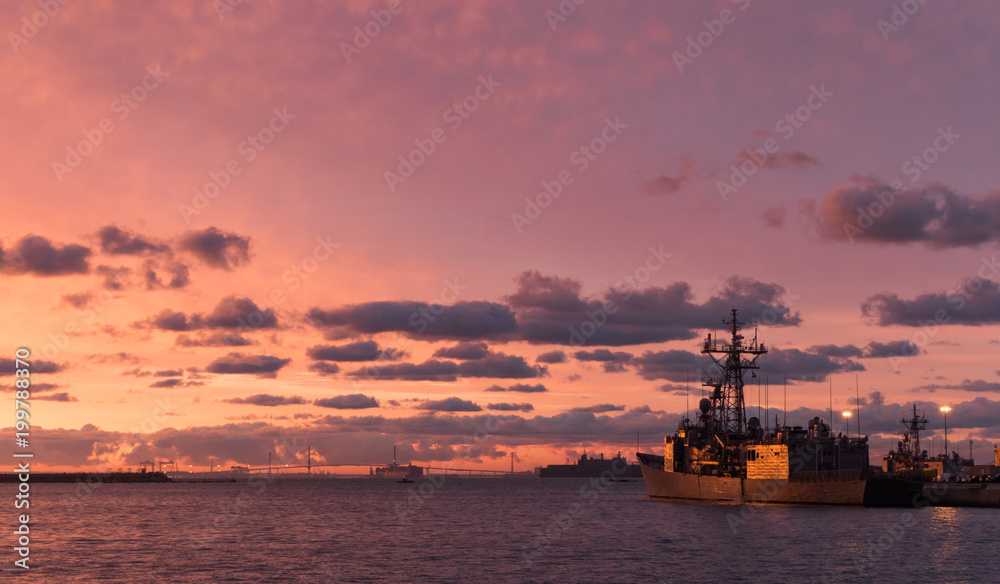 A background of a war ship in the naval base during sunset. Some navy ships in the sea with a marvelous orange light in the sky. 