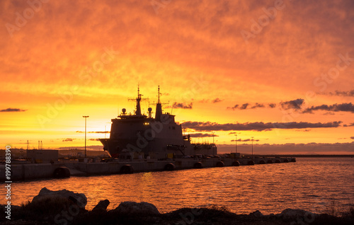 A background of a war ship in the naval base during sunset. Some navy ships in the sea with a marvelous orange light in the sky.  © Alejandro