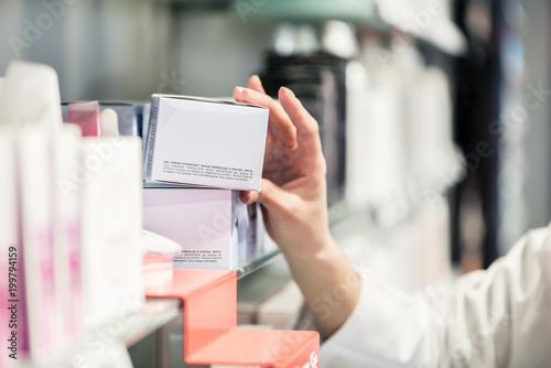 Close-up side view of the hand of a female pharmacist, picking up the package of the best pharmaceutical product from the shelf in a contemporary drugstore
