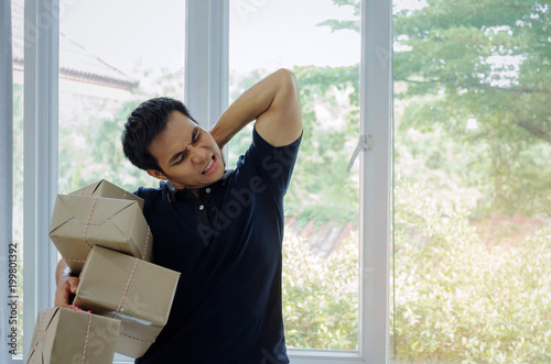 handsome young asian delivery man lifting many heavy packaging parcel box and be tired in home office, small business owner, cargo, mail, transportation, shopping online and shipping concept