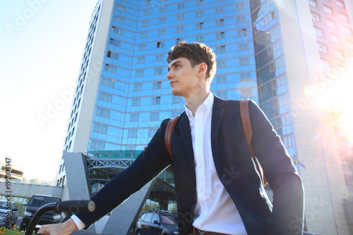 Confident young businessman walking with bicycle on the street in town. photo