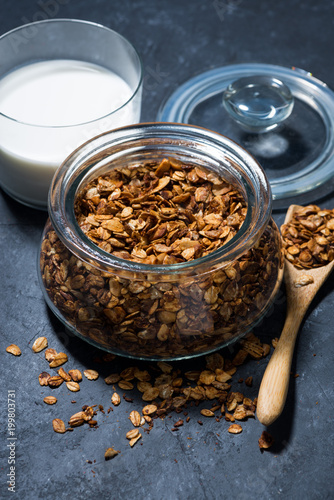 homemade baked granola in a glass jar on dark background, vertical top view