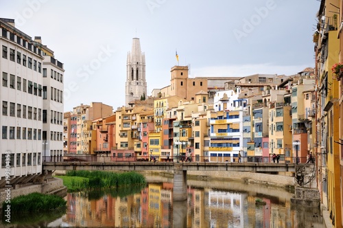 Colorful houses, reflected in the water of the river Onyar. View from the Red iron bridge or Girona Eiffel Bridge (Pont de les Peixateries velles). The historic Jewish quarter in Girona, Spain.  © Мария Аввакумова