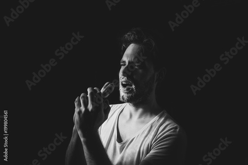 Young handsome man sing to shaving brush on black background. Black and white studio portrait.