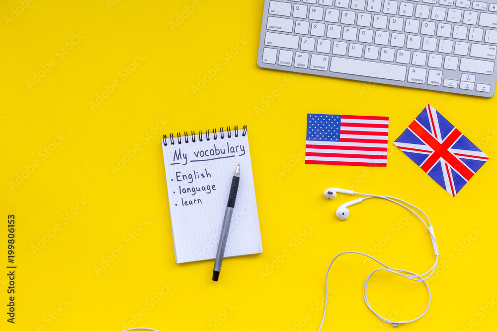 Learn english concept. British and american flags, computer keyboard, notebook for new vocabulary on yellow background top view copy space