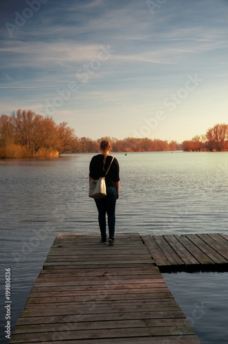 Blonde girl on a wooden landing stage overlooking a lake at sunset in Braunschweig, Germany © Ricardo