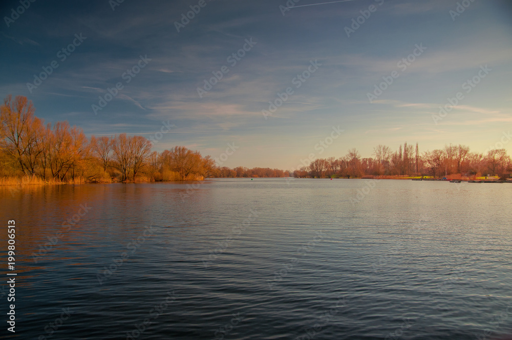 Fototapeta premium Panorama view of a lake with blue sky and golden sunset light. Südsee in Braunschweig, Germany