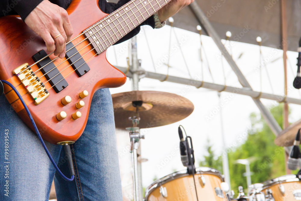 Musical band perfom on an open air festival. Bass guitarist man playing close, drums blurred Musical band perfom on an open air festival. Bass guitarist man playing close, drums blurred