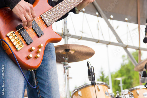 Musical band perfom on an open air festival. Bass guitarist man playing close, drums blurred
