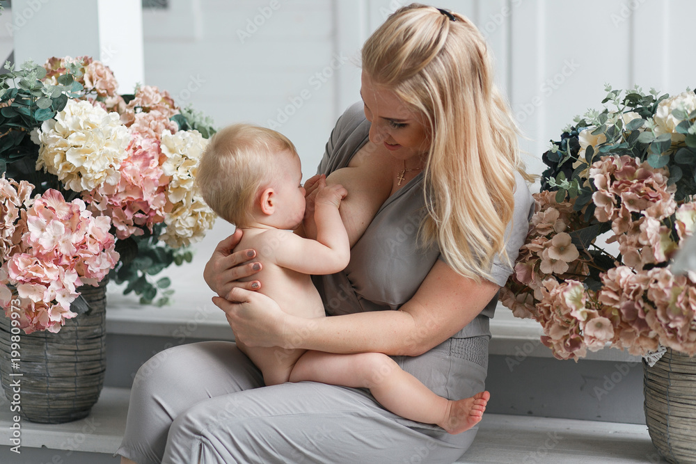 Young beautiful blonde mother breastfeeding her baby in decorated studio  room. Big breast Stock Photo