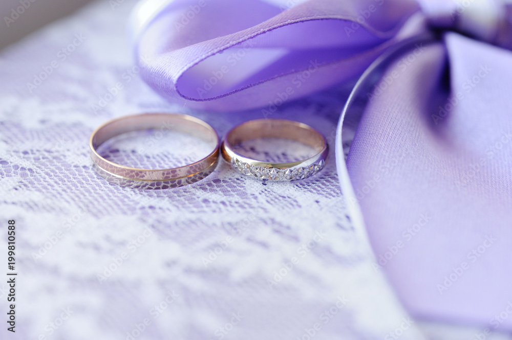 Wedding rings on a white fabric with lace near a bow of purple and white ribbon. Wedding rings on a white fabric with lace near a bow of purple and white ribbon.