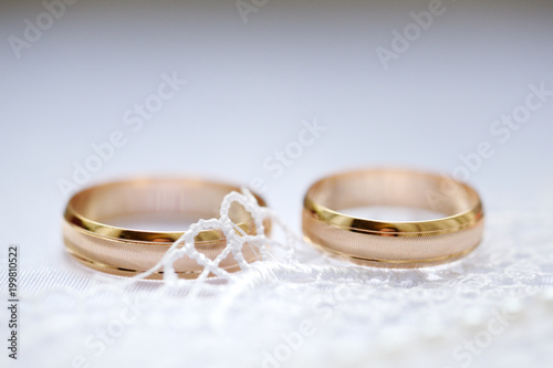 Gold wedding rings on a white fabric with lace and beads. Close-up.