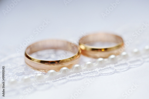 Gold wedding rings on a white fabric with lace and beads. Close-up.