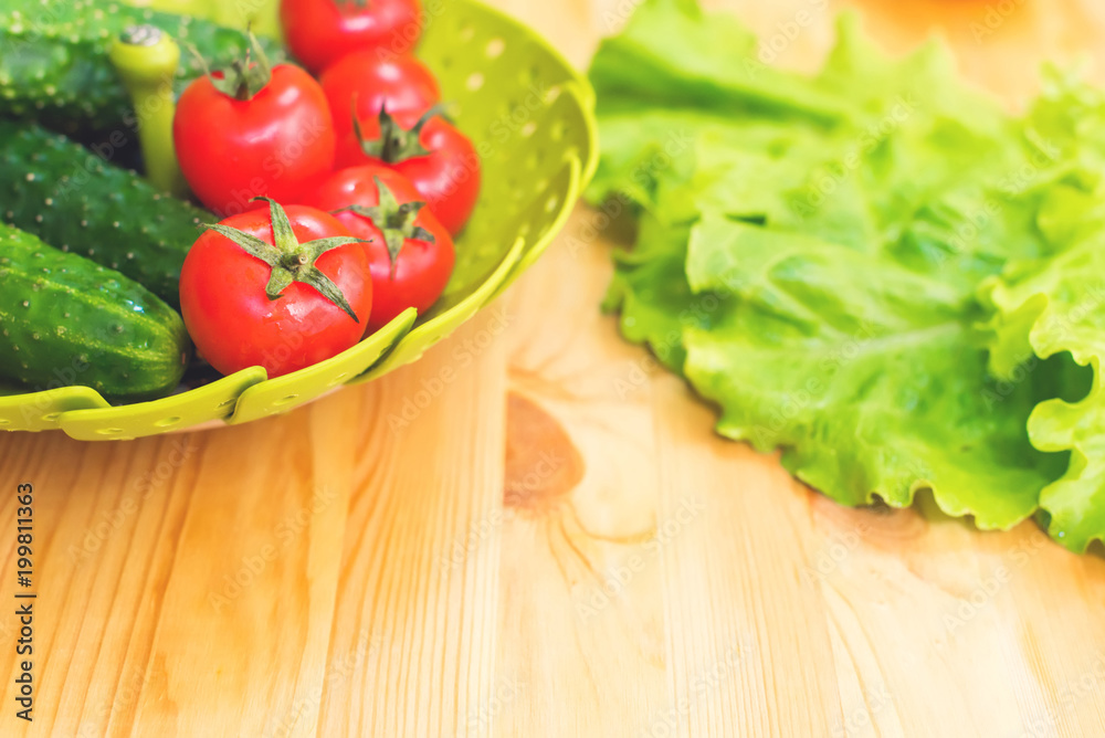 Fresh vegetables cucumbers and tomatoes in a green bowl on a wooden table next to green lettuce leaves. Vegetarian diet. Healthy diet and lifestyle