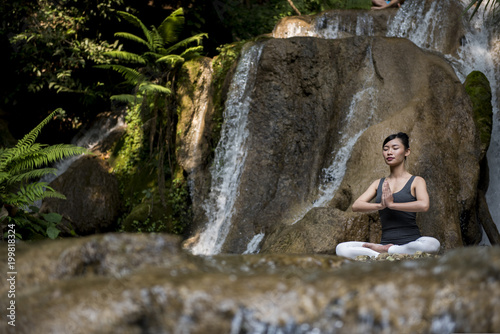 Young woman meditating in yoga pose near waterfall