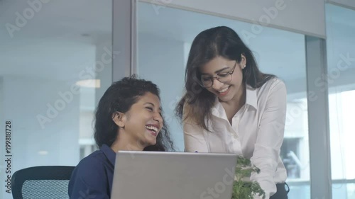 Two hard working and attractive female coworkers or office workers are smiling and enjoying their work while working on an  important project or task in a modern corporate office space