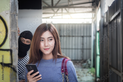 Beautiful young woman holding smartphone and being stalked by man criminal with the knife