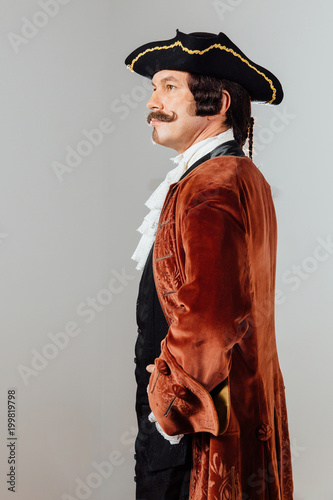 mustachioed eccentric man in the vintage clothes of the baron. Hat tricorn, brown jacket.