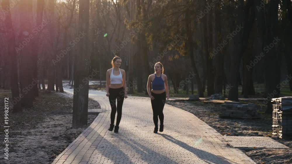 Two athletic woman running outdoors in slow motion on concrete track in park. Healthy fitness concept