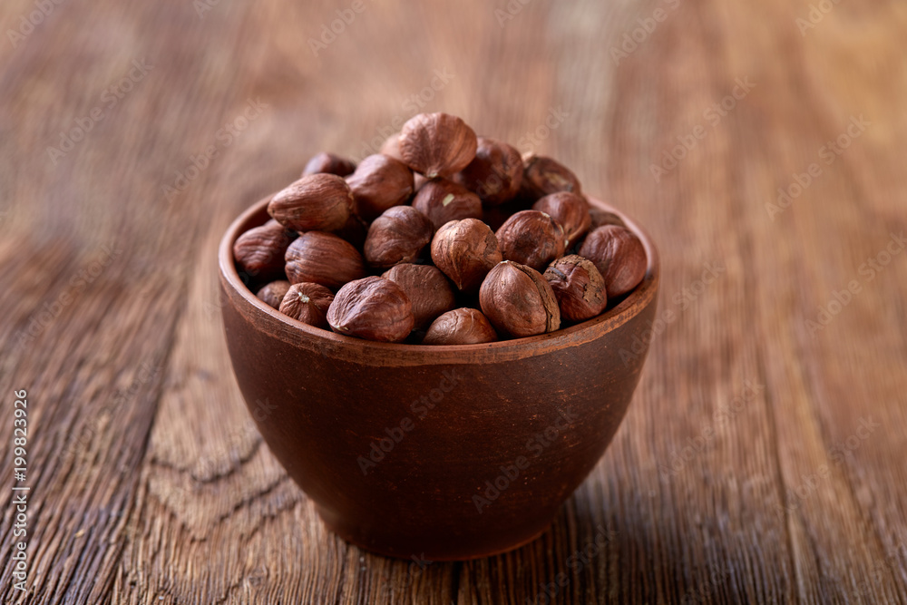 Hazelnuts in overturned ceramic bowl on wooden background with copy space, top view, selective focus. Hazelnuts in overturned ceramic bowl on wooden background with copy space, top view, selective focus.