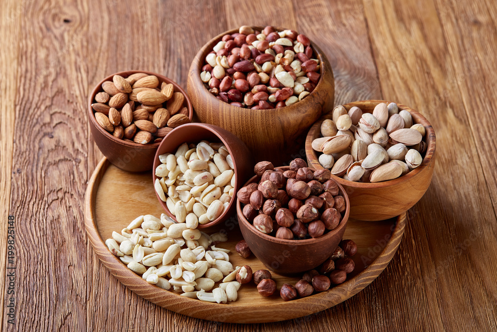 Mixed nuts arrenged on wooden tray over rustic background, close-up, selective focus.