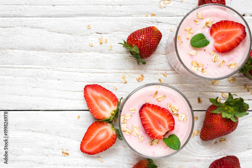 healthy strawberry yogurt with oats and mint in glasses with fresh berries over white wooden table