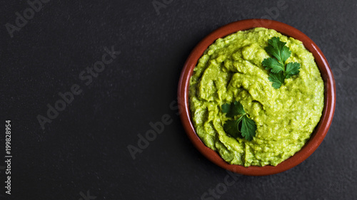 Guacamole spread  in clay bowl on a black background. Avocado sauce. Top view with copy space.