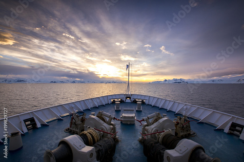 The bow of a ship appears as though it has sailed into a new world, as the spectacular sunset illuminates the sky over the mountains and glaciers of Antarctica.