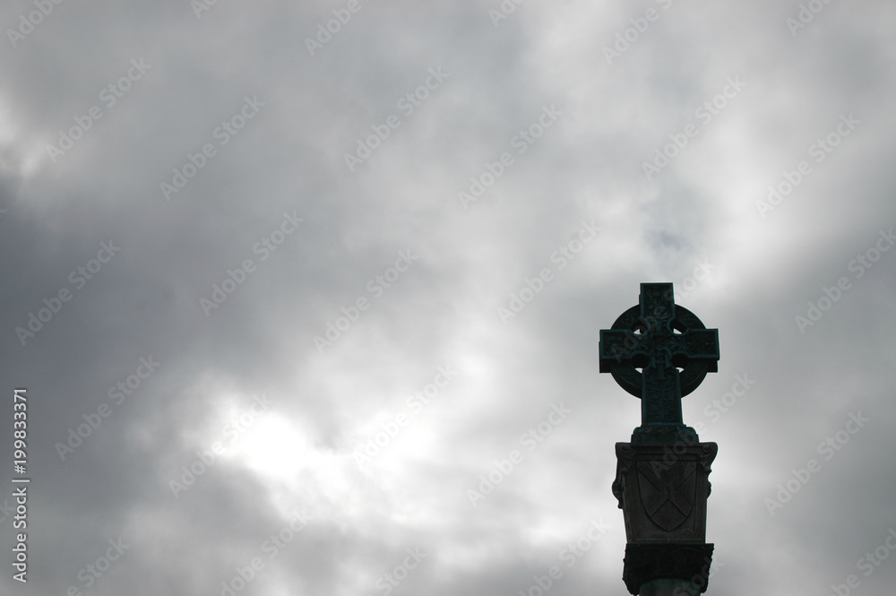 Celtic stone cross silhouetted against a soft grey cloudy sky