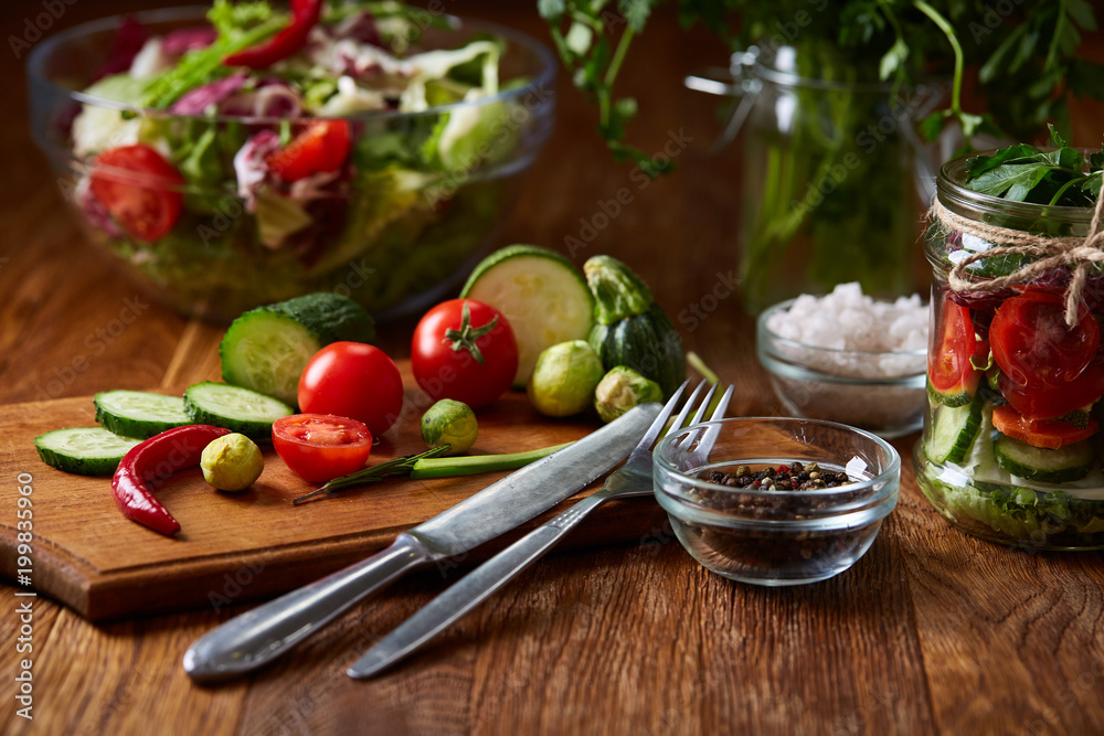 Delicious vegetable salad in jar and fresh veggies on cutting board on table, selective focus, close-up Delicious vegetable salad in jar and fresh veggies on cutting board on table, selective focus, close-up