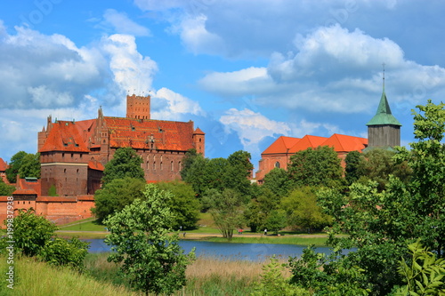 Malowniczy widok zamku krzyżackiego w Malborku, Polska, z przeciwnego brzegu rzeki Nugat, z malowniczymi obłokami na błękitnym niebie