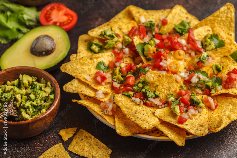 Mexican food concept. Nachos - yellow corn totopos chips with various sauces in wooden bowls: guacamole, cheese sauce, pico del gallo Mexican food concept. Nachos - yellow corn totopos chips with various sauces in wooden bowls: guacamole, cheese sauce, pico del gallo
