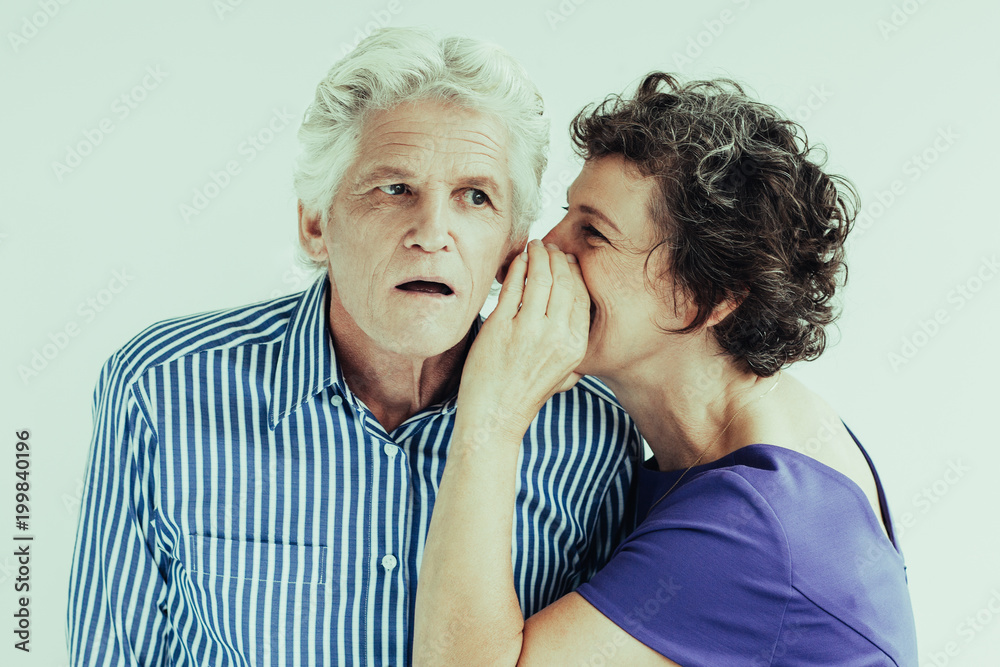 Foto Stock Mature woman telling secret to husband. She whispering in his  ear. Surprised senior man attentively listening to wife. Studio shot.  Relationship or gossip concept | Adobe Stock