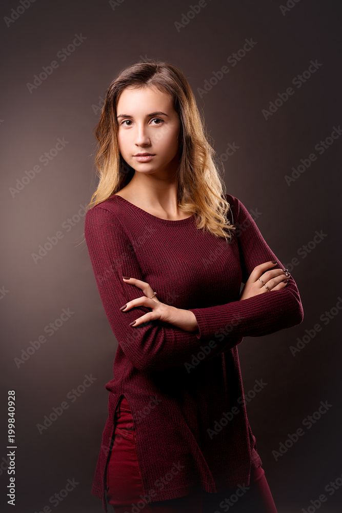 A stylish girl in dark red clothes crossed on her chest against a dark background. A stylish girl in dark red clothes crossed on her chest against a dark background.