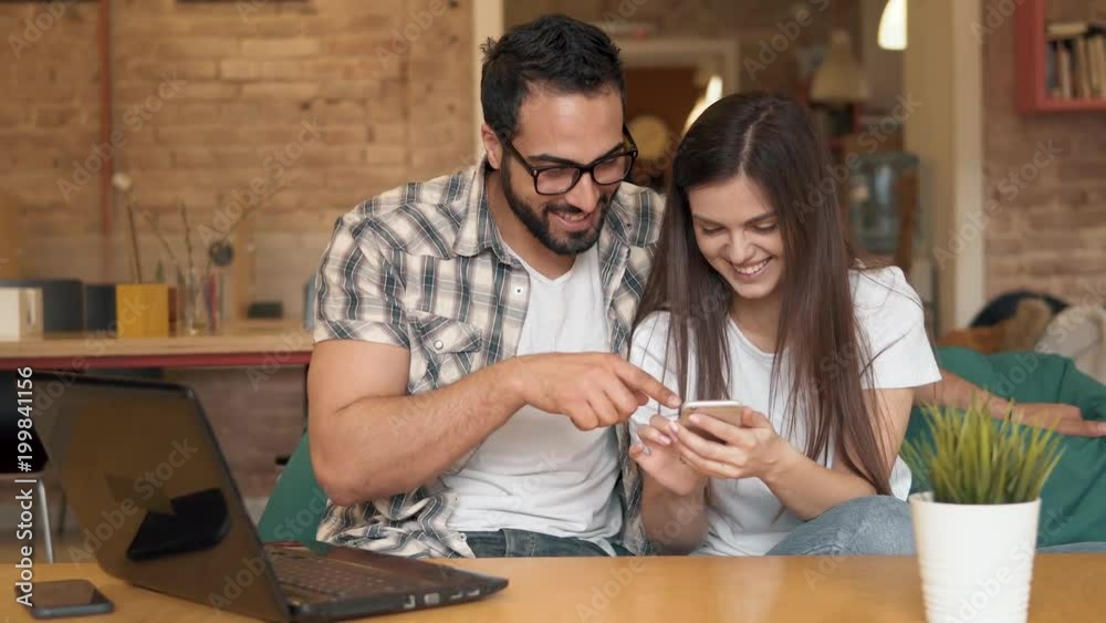 Couple discussing made photos while looking at them on phone, having lots of positive emotions with funny pictures on gadget, sitting on green comfortable chair in lovely modern cafe Couple discussing made photos while looking at them on phone, having lots of positive emotions with funny pictures on gadget, sitting on green comfortable chair in lovely modern cafe