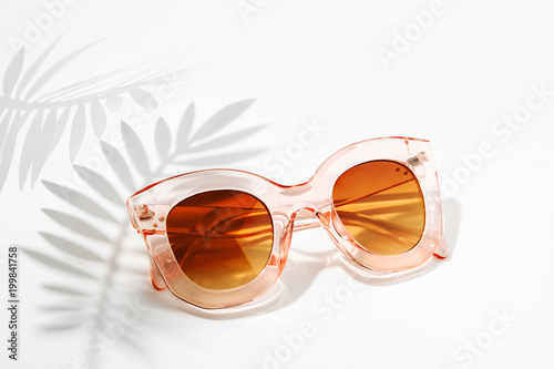 Stylish sunglasses with bright sunlight and shadow from palm leaves. Summer vacation concept.