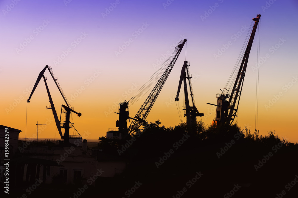 Silhouette of of cargo cranes. Port wharf landscape. Bright sunset, bright sky. Evening in the port