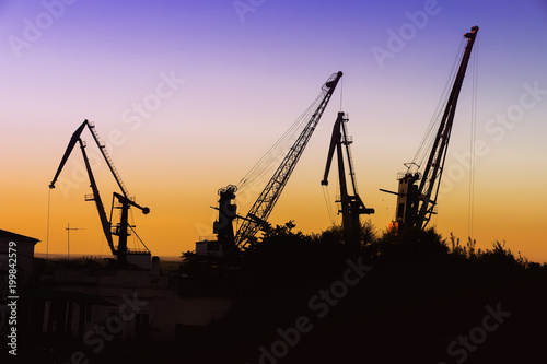 Silhouette of of cargo cranes. Port wharf landscape. Bright sunset, bright sky. Evening in the port