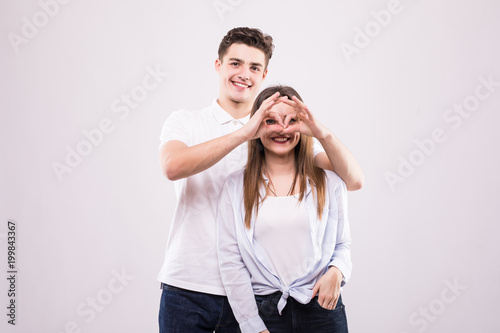 Concept of having funtime and grimacing, behaving like kids. Close up photo of two happy people making binoculars with their hands and showing tongues isolated on grey background