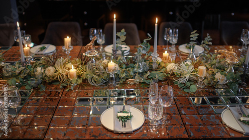 Mirror table served with plates, forks, spoons, glasses, napkins in the restaurant. Beautiful festive table decorated with fresh flowers and candles