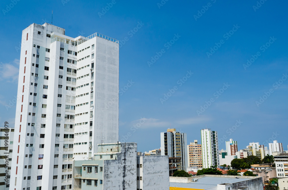 Large white building and full of windows in the foreground, in the background many buildings and a large, clean blue sky.