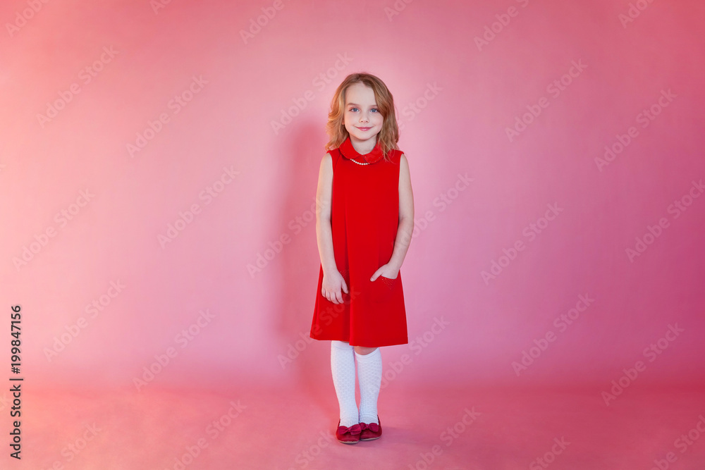Little cute sweet smiling girl in red dress standing on pink colourful pastel trendy modern fashion pin-up background Little cute sweet smiling girl in red dress standing on pink colourful pastel trendy modern fashion pin-up background