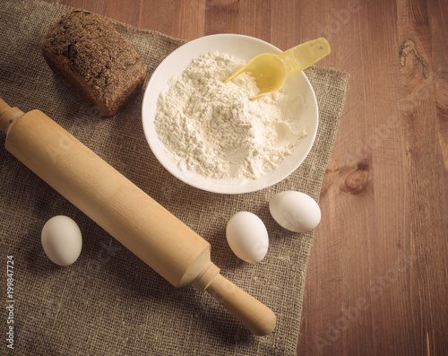 Eggs, bread, flour and kitchen tools on a wooden board