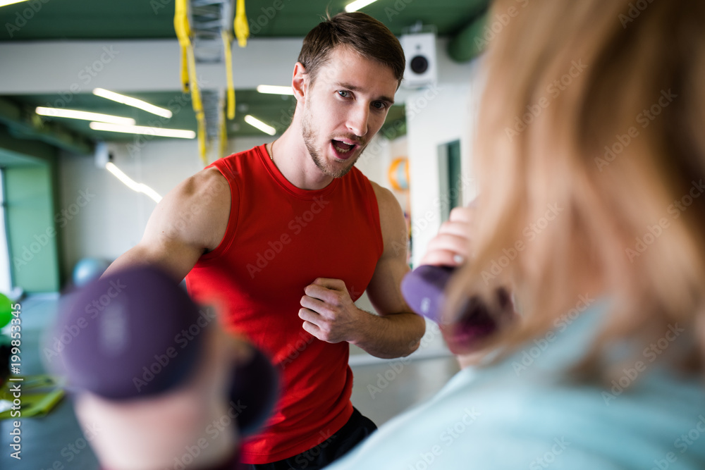 Portrait of handsome personal trainer motivating young woman training with dumbbells in gym, copy space Portrait of handsome personal trainer motivating young woman training with dumbbells in gym, copy space