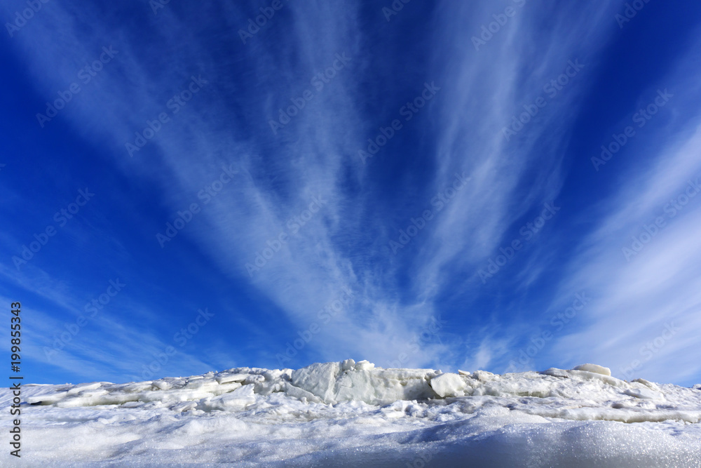 bright blue spring sky with cirrus clouds over melting ice and snow..