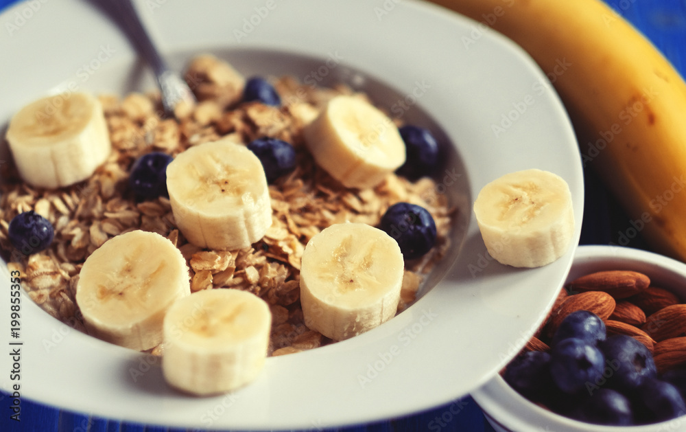 Healthy eating, food and diet concept - oatmeal with berries, nuts and bananas, white plate, blue wooden background.