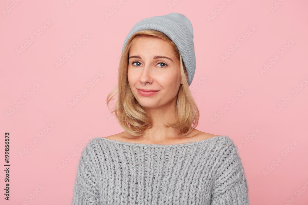 Ok! Portrait of young blonde woman smiles with irony to her husband. Wears casual sweater and cap. Isolated over pink background Ok! Portrait of young blonde woman smiles with irony to her husband. Wears casual sweater and cap. Isolated over pink background