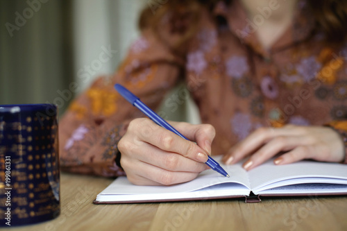 Close up of business woman writing notes in notebook; selective focus background. 
