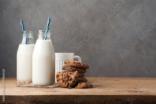 Two bottles of milk and chocolate chip cookies on dark background with copy space photo